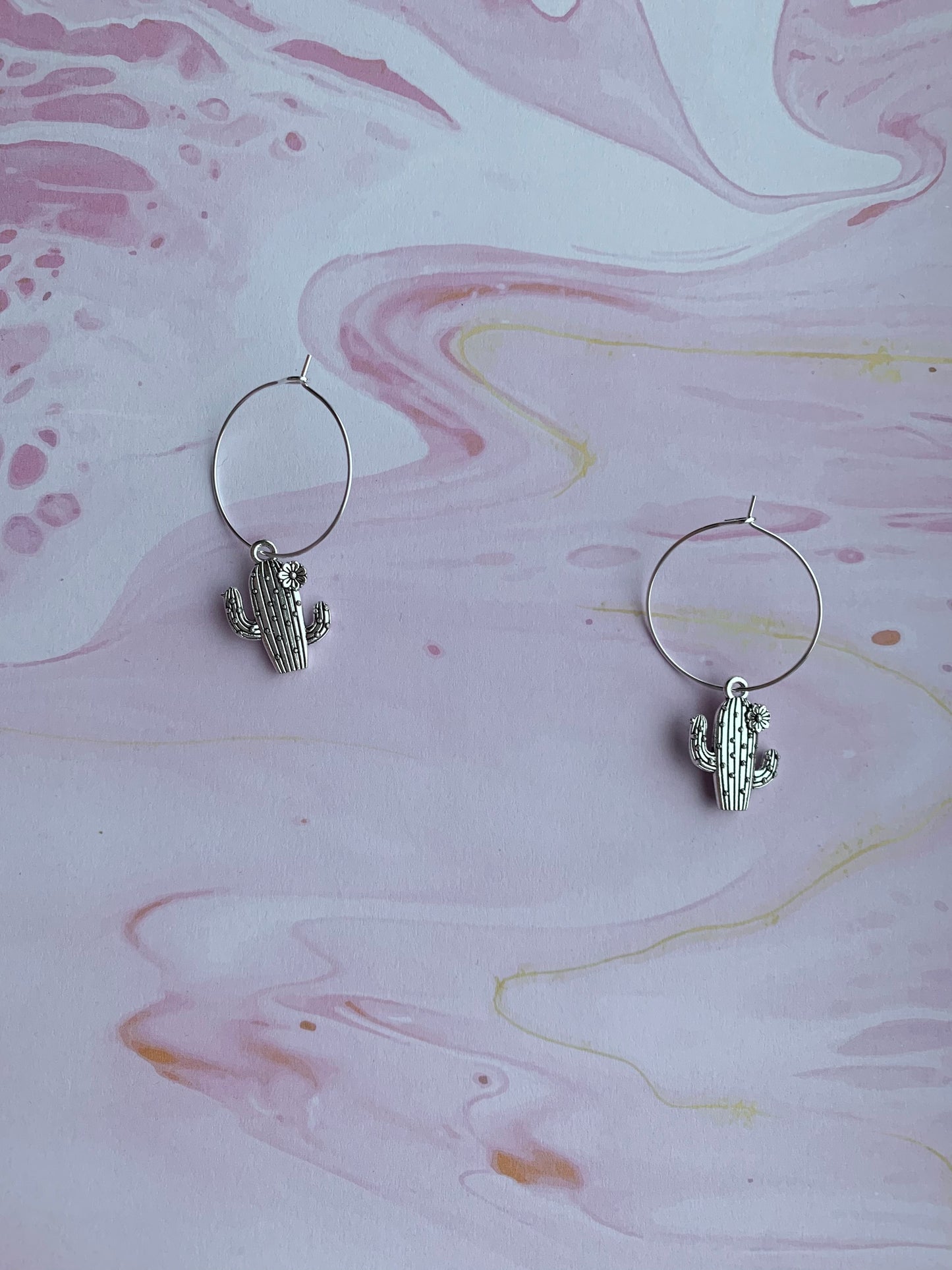Dangly novelty earrings. Silver coloured alloy cacti charms with spikes and flower on silver plated hoops. Cheap cute earrings.