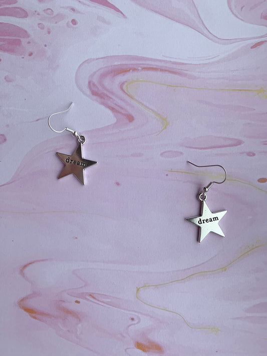 Large star silver coloured alloy charm with the word dream embossed across the centre on silver plated hooks. Hamilton earrings. Dream earrings.
