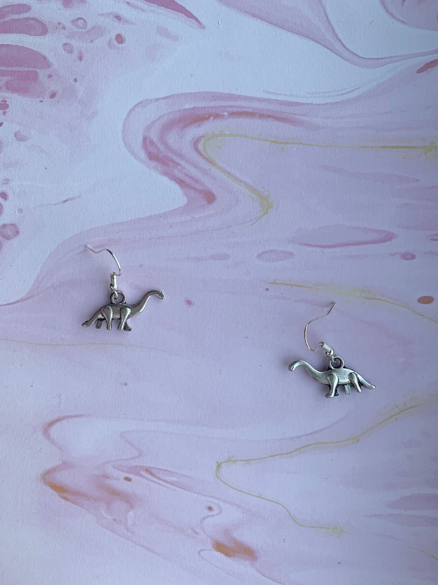 Alloy metal silver coloured brontosaurus charm on silver plated hoops. Dinosaur earrings. Animal earrings. Novelty earrings. 