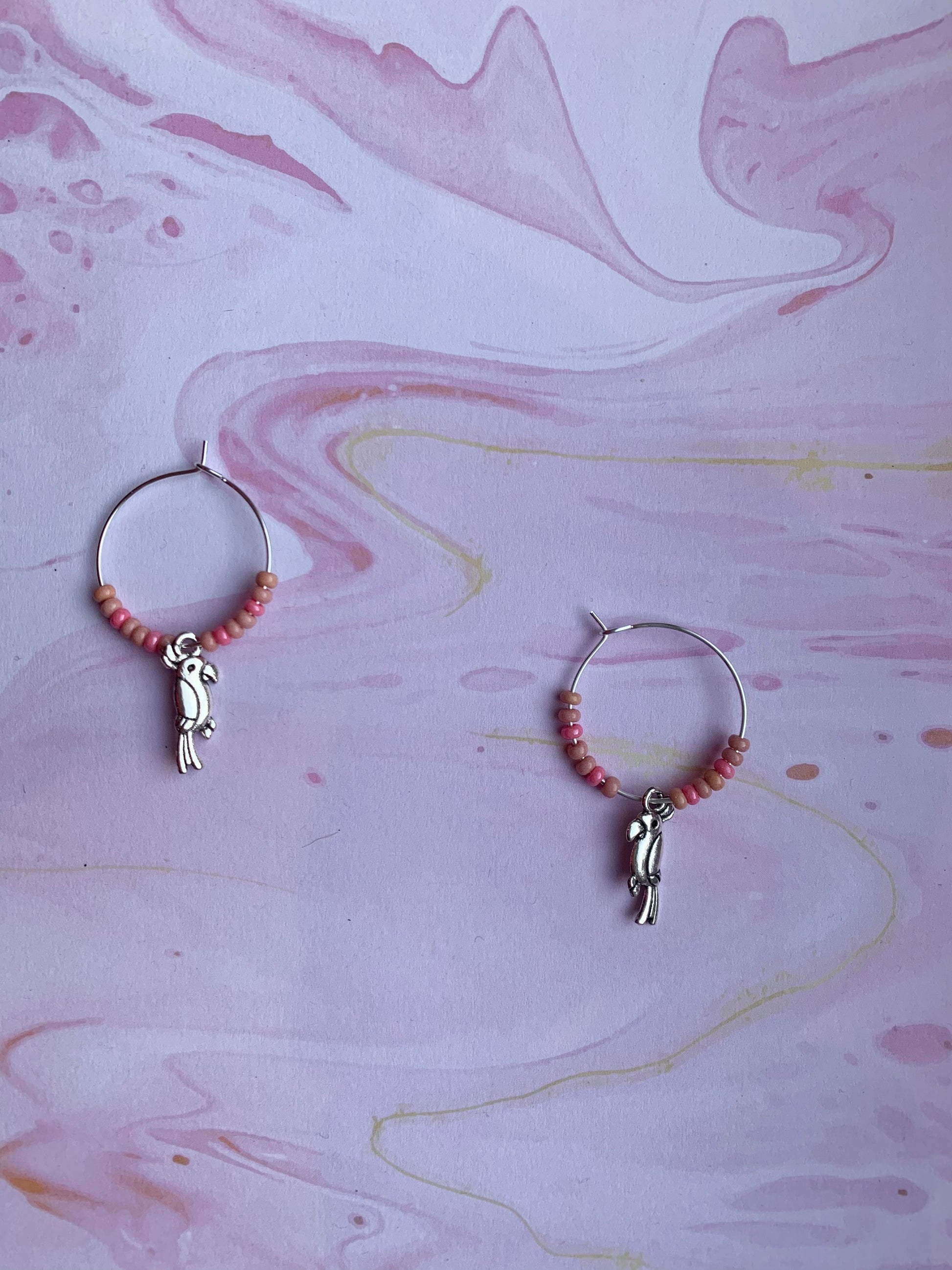 Colourful hoop earrings. Each pair has a alloy silver coloured parrot charm on silver plated hoops with different colour themed seed beads on the hoops. There is a white sparkle, turquoise and pink coral pair. Animal earrings. Bird earrings. 