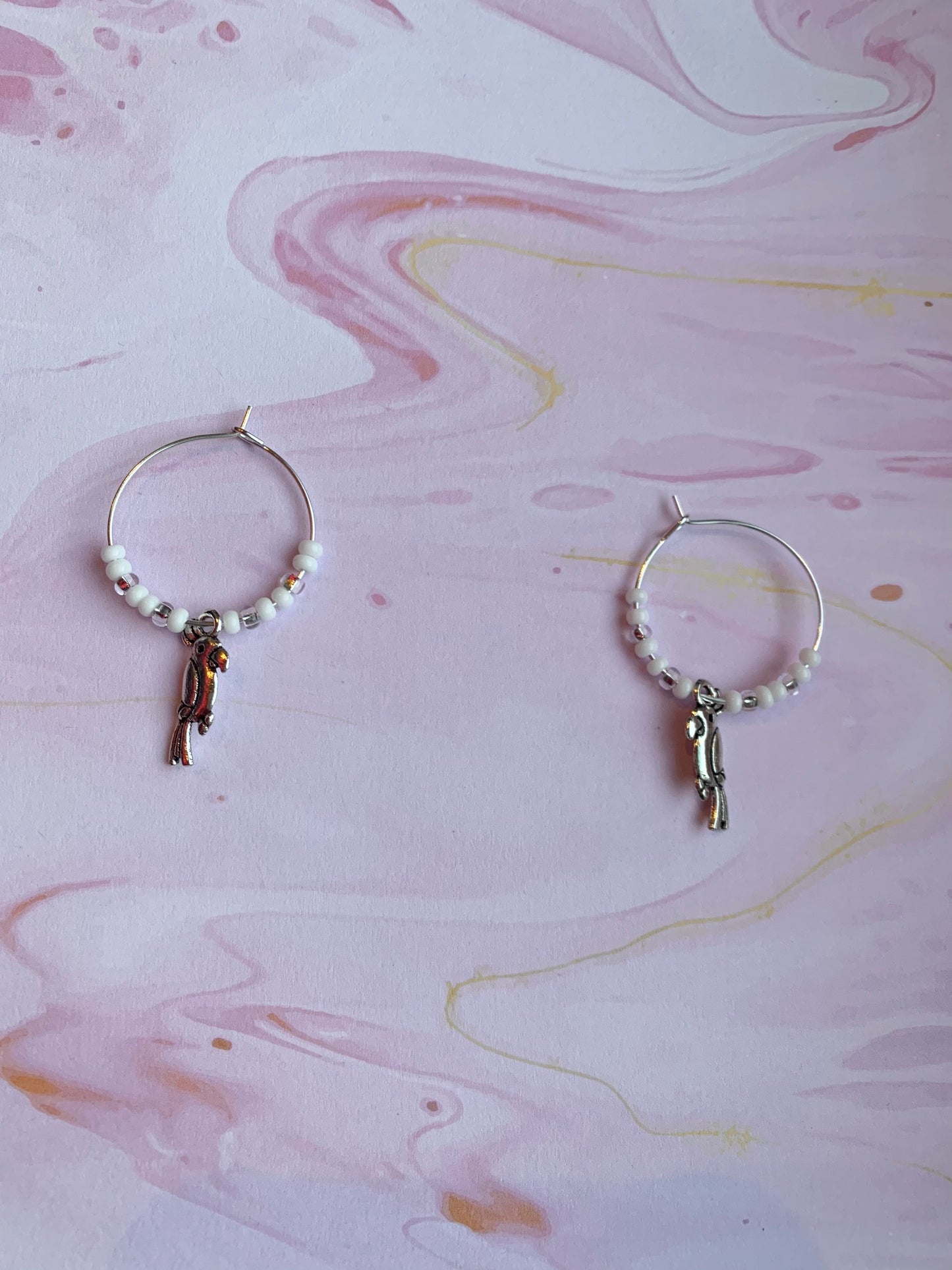 White parrot earrings. Colourful hoop earrings. Each pair has a alloy silver coloured parrot charm on silver plated hoops with different colour themed seed beads on the hoops. There is a white sparkle, turquoise and pink coral pair. Animal earrings. Bird earrings. 