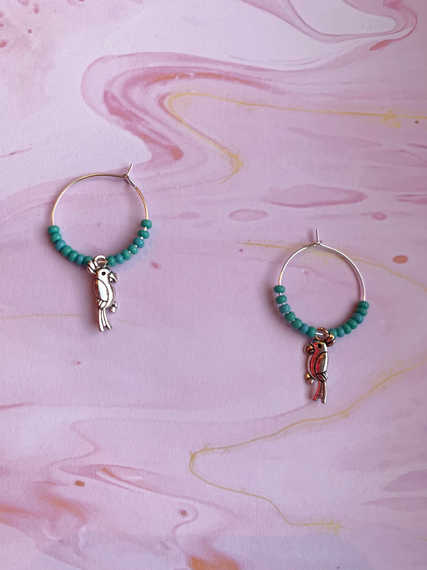 Turquoise parrot earrings. Colourful hoop earrings. Each pair has a alloy silver coloured parrot charm on silver plated hoops with different colour themed seed beads on the hoops. There is a white sparkle, turquoise and pink coral pair. Animal earrings. Bird earrings. 