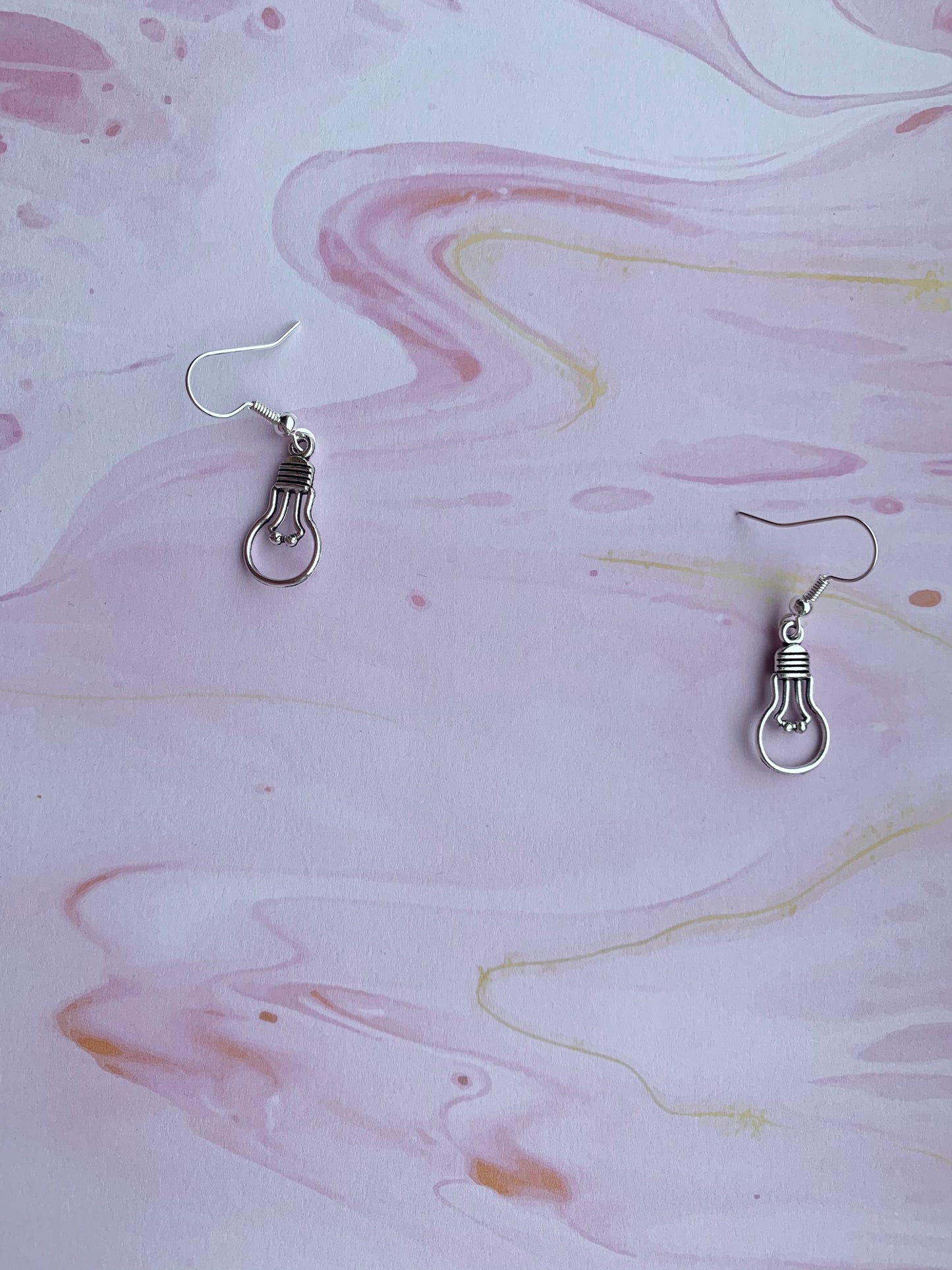 An alloy silver coloured charm that is the outline of a round light bulb on silver plated hooks. Novelty earrings. Great gift for people that are creative or writing a book. 