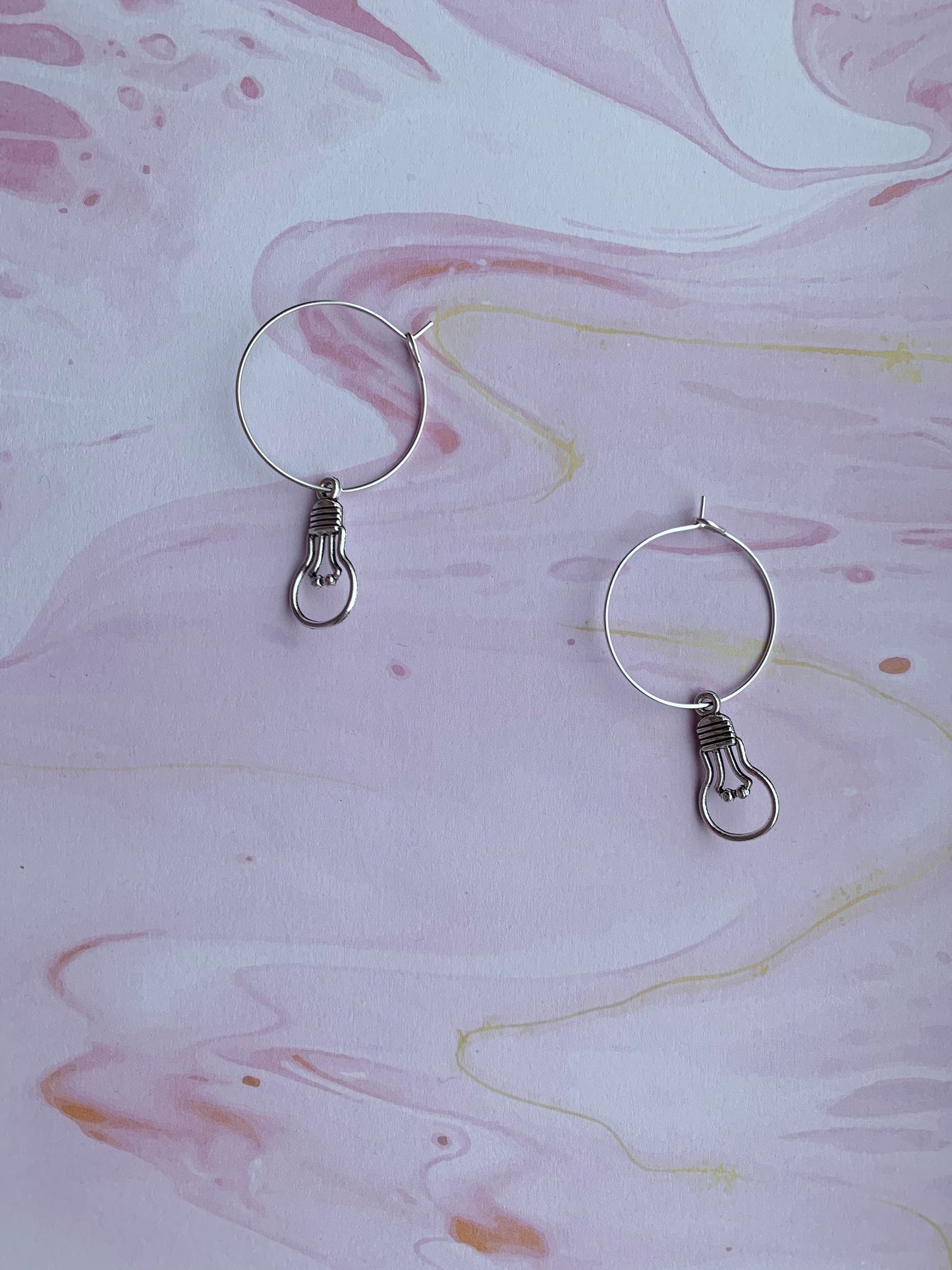 An alloy silver coloured charm that is the outline of a round light bulb on silver plated hoops. Novelty earrings and perfect for thinking of ideas. Great gift for people that are creative or writing a book. 