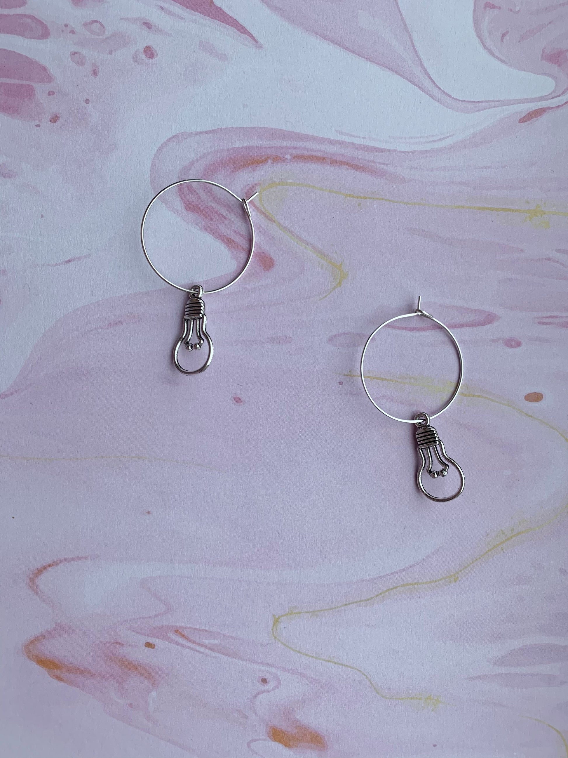 An alloy silver coloured charm that is the outline of a round light bulb on silver plated hoops. Novelty earrings and perfect for thinking of ideas. Great gift for people that are creative or writing a book. 