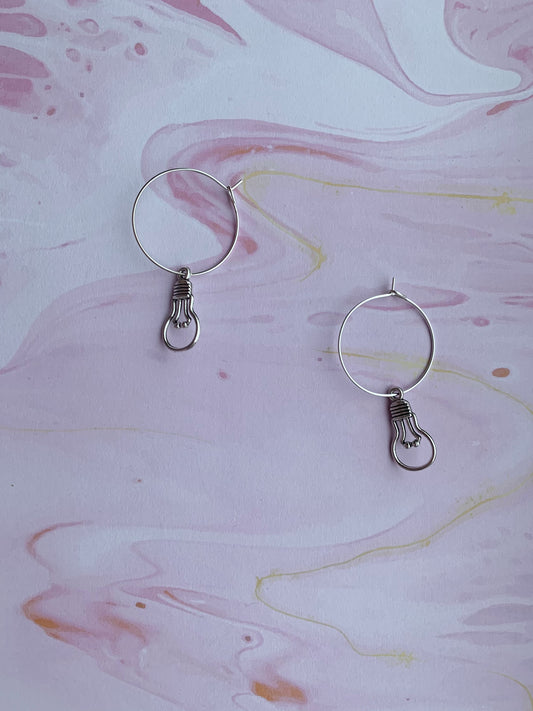 An alloy silver coloured charm that is the outline of a round light bulb on silver plated hoops. Novelty earrings and perfect for thinking of ideas. Great gift for people that are creative or writing a book. 