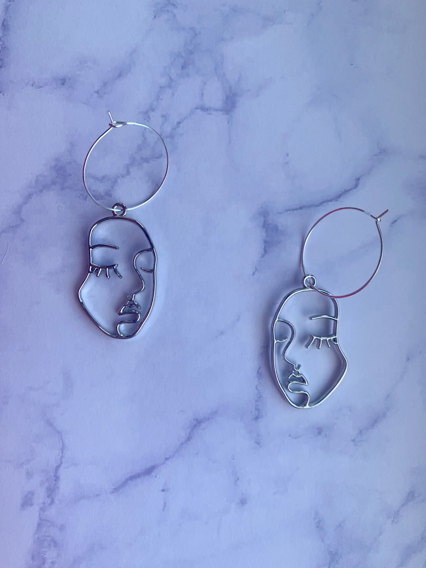 Beautiful female face outline in silver alloy metal on silver plated hoops earrings. Beautiful earrings. Earrings for women. Earrings for sale. hoop earrings. silver earrings. 