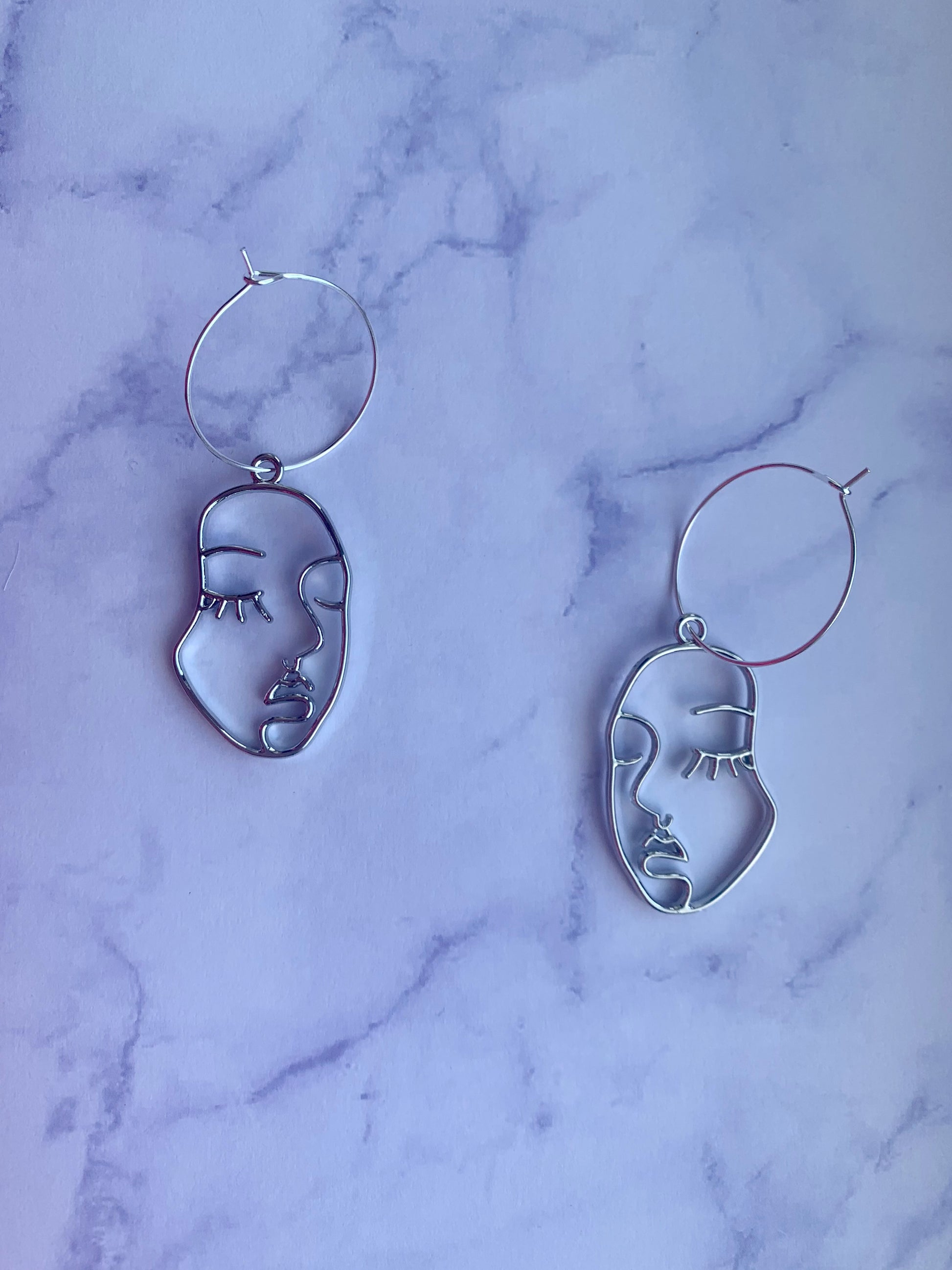 Beautiful female face outline in silver alloy metal on silver plated hoops earrings. Beautiful earrings. Earrings for women. Earrings for sale. hoop earrings. silver earrings. 